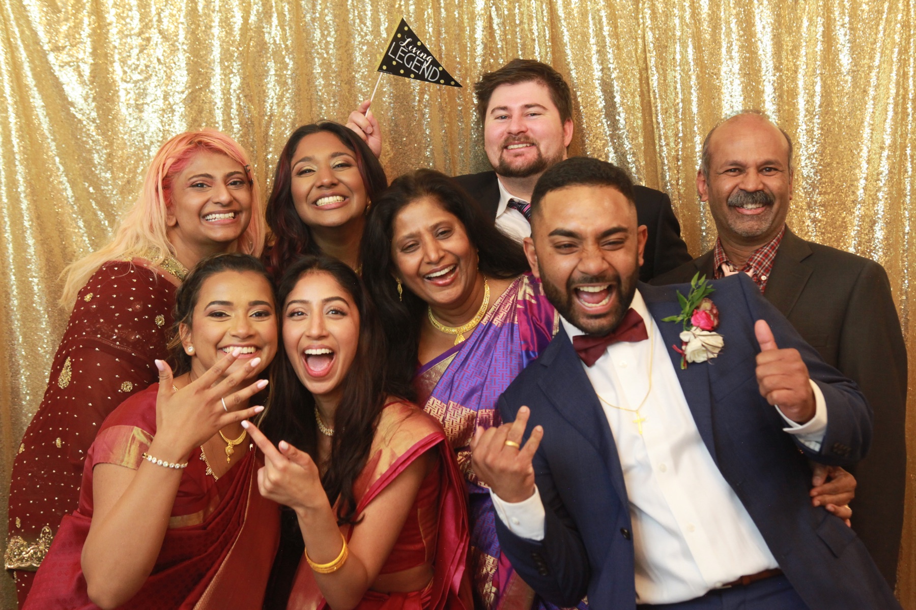 A wedding party gathers in front of a gold backdrop