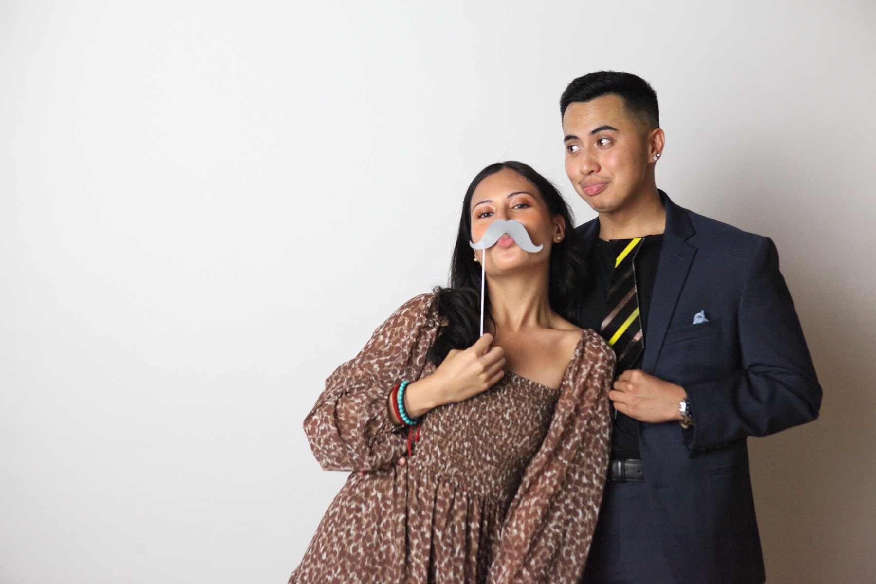 A couple pose with a moustache prop